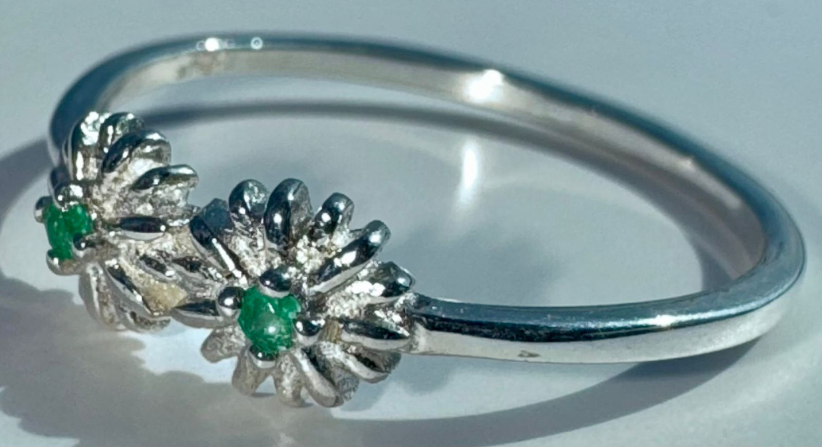 Anillo CASSIRA en forma de flor de plata 925 con dos esmeraldas redondas naturales colombianas de 1.5mm y 0.08ct cada una. Talla 7.5 US